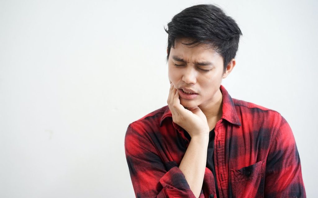 Young man holding his jaw in pain TMJ treatment restorative dentistry dentist in Gaithersburg Maryland